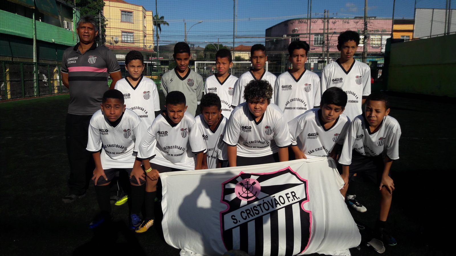 Turma da Escolinha do Tio Alexandre perfilada com a bandeira do São Cristóvão de Futebol e Regatas